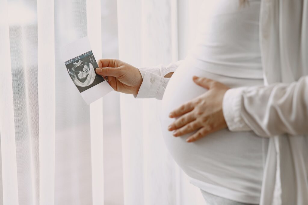 pregnant-woman-standing-by-window-looking-photo