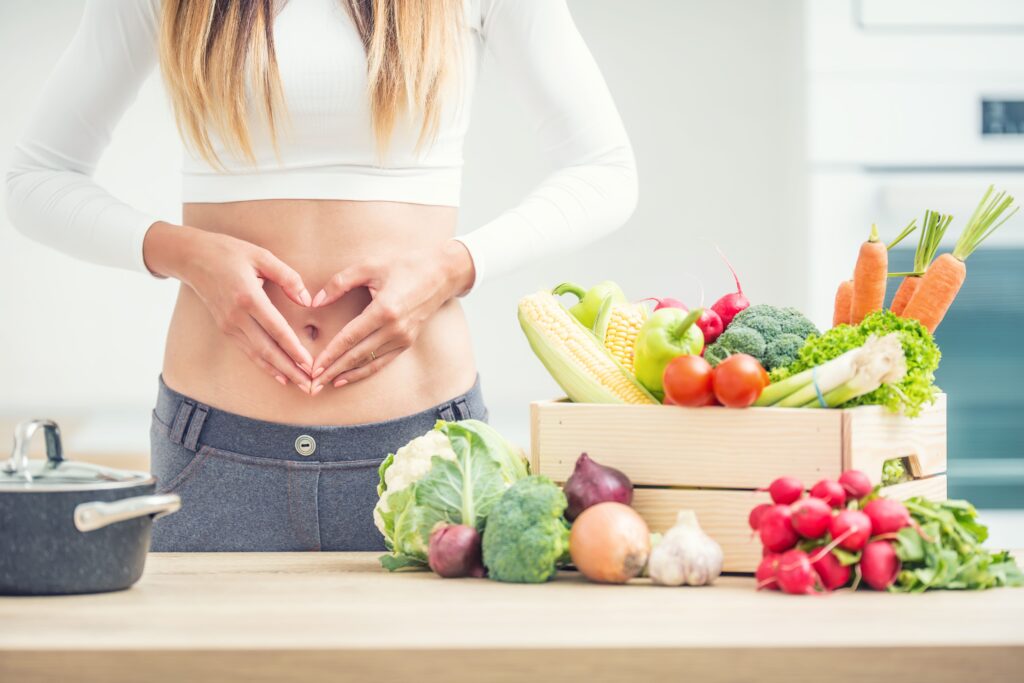 woman-with-sports-figure-her-belly-shows-heart-shape-home-kitchen-with-wooden-box-full-organic-vegetable